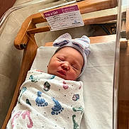 Violet joined the competition — help win amazing prizes! newborn, baby, sleeping, hospital, bassinet, blanket, footprint_pattern, hat, bow, wooden_bed, crib, infant, wrapped, peaceful, face, person, cute, portrait, indoor, resting