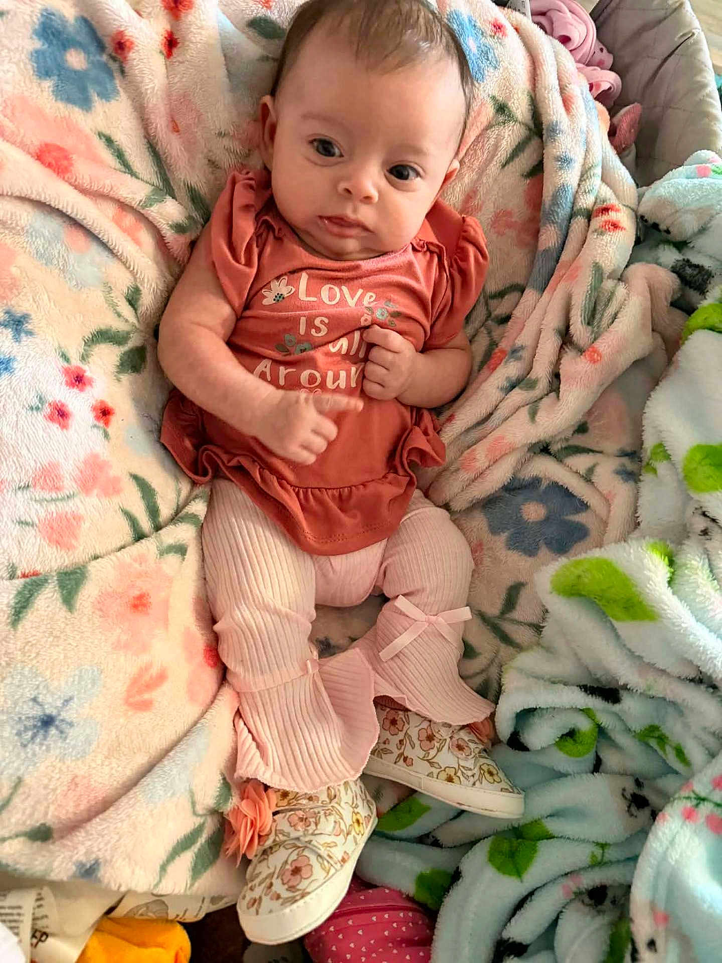 Nova is registered to the contest to win money with this photo: baby, infant, blanket, floral_pattern, clothing, pink, shoe, footwear, cute, child, person, portrait, soft_texture, comfort, indoors, laying_down, baby_girl, fabric, pattern, warm