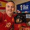 casual, celebration, dog, fifa_world_cup, flag, happy, home_interior, indoor, man, pet, photography, portrait, red_clothing, smiling, soccer_ball, soccer_jersey, spain_flag, sports_fan, trophy, tv_screen