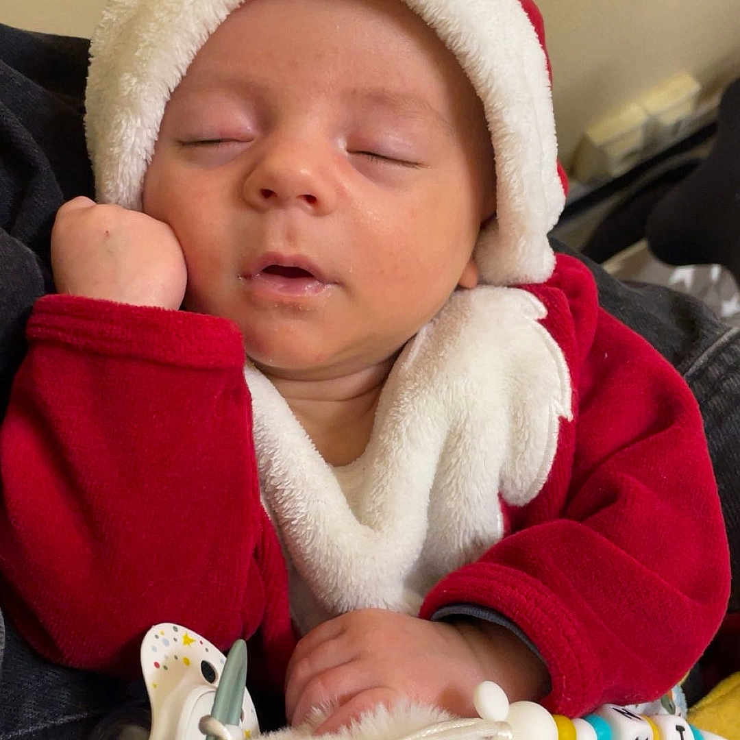 Austin a rejoint le concours — aidez-le/la à gagner de superbes lots ! baby, blanket, child, comfort, cozy, cute, face, hand, holiday_outfit, indoors, infant, pacifier, portrait, red_clothing, resting, santa_hat, sleeping, soft_toy, warm, white_fur