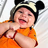 baby, smiling, infant, hat, mickey_mouse, orange_shirt, bracelet, happy, lying_down, white_background, measuring_scale, cute, child, portrait, close_up, clothing, headwear, person, baby_girl, baby_boy