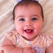 Melody is registered to the contest to win money with this photo: baby, child, smiling, face, headband, bow, flower, dress, floral, infant, cute, happy, soft_blanket, portrait, skin, hand, lying_down, indoors, closeup, person