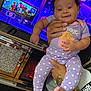 Lilly is registered to the contest to win money with this photo: baby, child, purple_clothing, polka_dot, tattoos, hand, television, tv_screen, animated_background, indoor, smiling, cute, feet, person_holding, purple, infant, screen, home, bright_colors, happy
