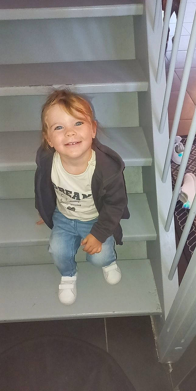 Mia participe au concours pour gagner de l'argent avec cette photo : baby_toddler_clothing, cheek, child, comfort, denim, floor, flooring, fun, hair, happy, hardwood, jeans, joy, person, shelf, sitting, sleeve, smile, sock, t_shirt