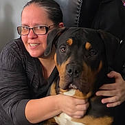 Rocky joined the competition — help win amazing prizes! woman, person, dog, rottweiler, pet, cuddle, hugging, smiling, glasses, indoors, portrait, close_up, black_clothing, leather_couch, brown_and_black, large_dog, canine, companion, happy, photography