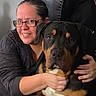 black_clothing, brown_and_black, canine, close_up, companion, cuddle, dog, glasses, happy, hugging, indoors, large_dog, leather_couch, person, pet, photography, portrait, rottweiler, smiling, woman