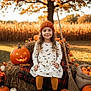 child, girl, pumpkin, jack_o_lantern, hay_bale, autumn, fall, orange, dress, knit_hat, broom, outdoor, smile, curly_hair, leaves, plaid_blanket, boots, field, tree, festive
