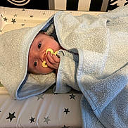 Theo is registered to the contest to win money with this photo: baby, pacifier, towel, blue, infant, wrapped, face, hand, changing_pad, stars, newborn, skin, cute, resting, indoors, soft_texture, hood, blanket, lying_down, comfort