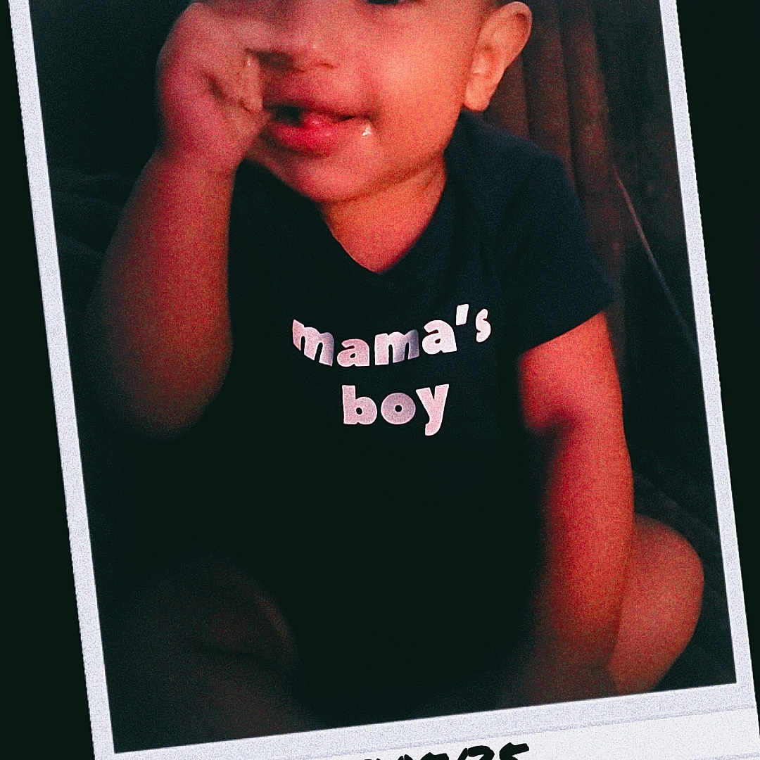 Zyair is registered to the contest to win money with this photo: baby, child, clothing, cute, dark_background, face, handwritten_date, happy, indoors, infant, mamas_boy, person, polaroid_frame, portrait, seated, smiling, text, thumbsucking, tshirt, young