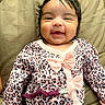 baby, child, infant, smiling, happy, portrait, face, sitting, leopard_print, pink_clothing, bow, onesie, padded_seat, cushion, indoor, close_up, dark_hair, brown_eyes, adorable, photography