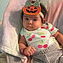 baby, child, infant, pumpkin_headband, cute, soft_cushion, cherry_pattern, shirt, pants, red_bracelet, indoor, portrait, expression, comfortable, seated, clothing, headwear, person, young, cozy