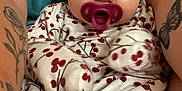 Raya is registered to the contest to win money with this photo: baby, pacifier, infant, tattoo, arm, clothing, pattern, red_berries, teal_shirt, skin, foot, toes, closeup, person, cute, child, young, comfort, holding, portrait