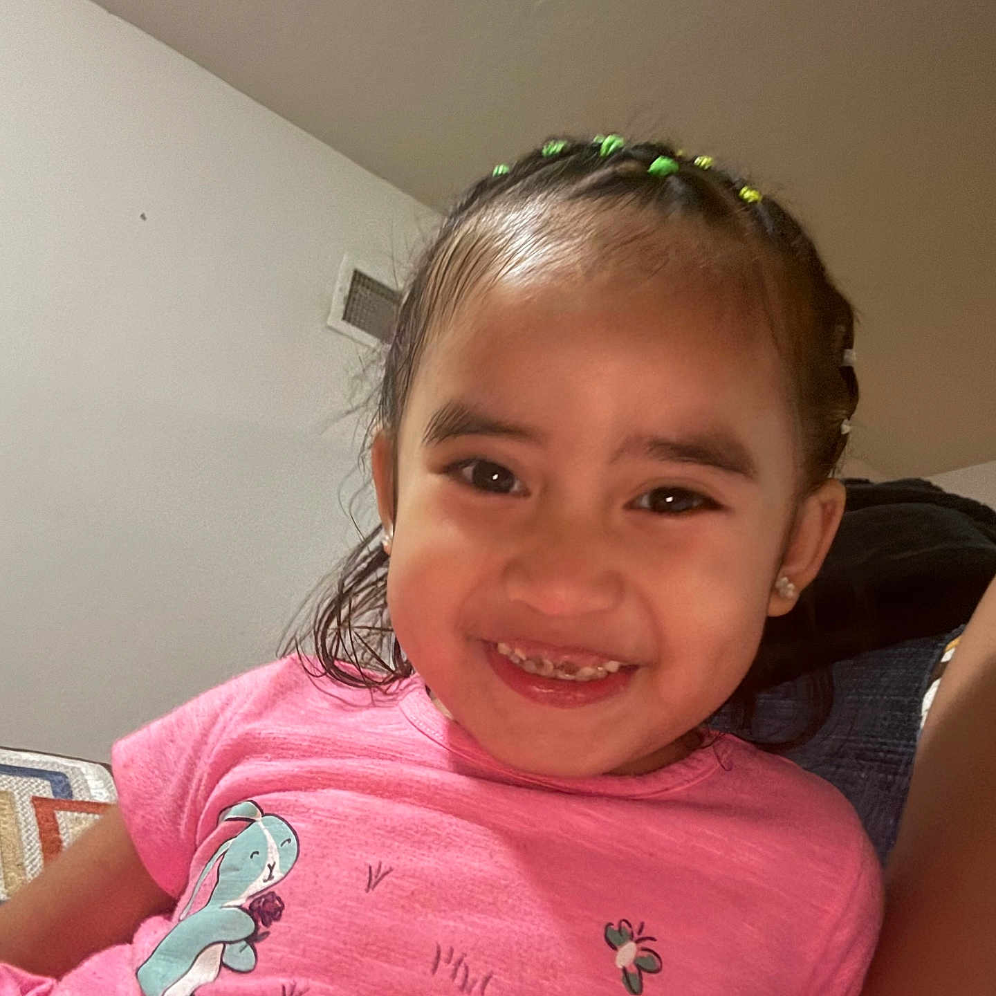 Ava joined the competition — help win amazing prizes! child, girl, smiling, portrait, indoors, pink_shirt, cartoon_shirt, hair_beads, braids, teeth, happy, sitting, closeup, face, eyes, earrings, furniture, home, casual, photography