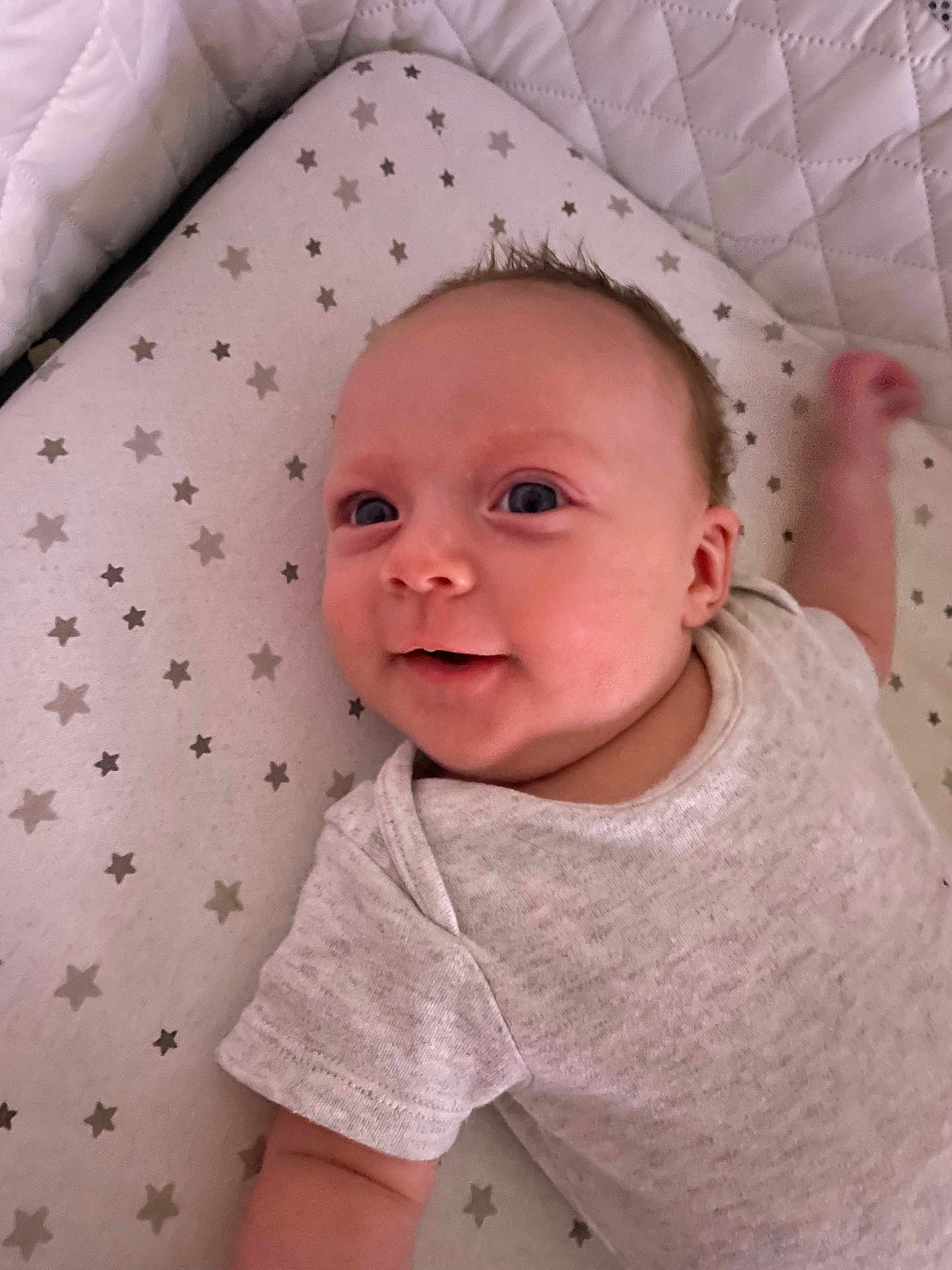 Ellie is registered to the contest to win money with this photo: baby, infant, smiling, onesie, lying_down, star_pattern, mattress, cute, child, young, face, skin, arm, happy, indoors, portrait, person, head, expression, baby_clothes