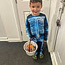 child, boy, costume, skeleton, halloween, candy, bucket, smile, indoor, carpet, door, keys, footwear, crocs, long_sleeve, pants, trick_or_treat, young, happy, holiday