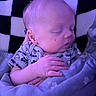 Haze is registered to the contest to win money with this photo: newborn, baby, sleeping, infant, portrait, face, closed_eyes, blanket, onesie, clothing, hands, cuddled, cozy, indoors, checkered_background, purple_lighting, seated, relaxed, soft_fabric, photography