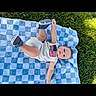 Hudson is registered to the contest to win money with this photo: baby, blanket, grass, outdoor, child, infant, blue, white, footwear, american_flag, cute, young, clothing, person, summer, sunlight, nature, lying_down, happy, playful