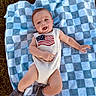 baby, infant, blanket, checkered, outdoor, grass, smile, happy, onesie, american_flag, shoe, footwear, lying_down, child, portrait, cute, young, person, summer, sunlight