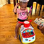toddler, child, indoor, toy_car, party_hat, drum, purple_drumstick, pink_shirt, wooden_floor, furniture, chair, floor, playtime, cute, baby, smiling, person, celebration, colorful_toy, happy