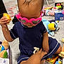 toddler, child, indoor, toys, sunglasses, pink, heart_shaped, carpet, playtime, blue_dress, hand, toy_figure, stuffed_animal, floor, person, casual_clothing, playroom, candid, cute, baby