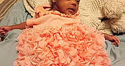 Zia is registered to the contest to win money with this photo: baby, infant, pink_dress, blanket, bed, pillow, sleepy, indoor, person, portrait, cute, child, soft_texture, cozy, relaxed, newborn, clothing, skin, head, lying_down