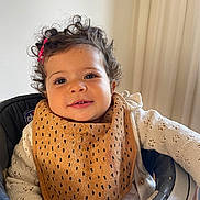 Inaya a rejoint le concours — aidez-le/la à gagner de superbes lots ! toddler, child, curly_hair, pink_hair_clip, bib, knitted_sweater, high_chair, smile, face, hand, indoors, window, curtain, baby, person, clothing, seated, happy, home, portrait