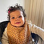 toddler, child, curly_hair, pink_hair_clip, bib, knitted_sweater, high_chair, smile, face, hand, indoors, window, curtain, baby, person, clothing, seated, happy, home, portrait