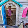 child, toddler, girl, playhouse, outdoor, patio, pink_clothing, sandal, standing, portrait, face, playground, plastic_toy, blue_door, pink_shutters, backyard, house, sunlight, furniture, playtime
