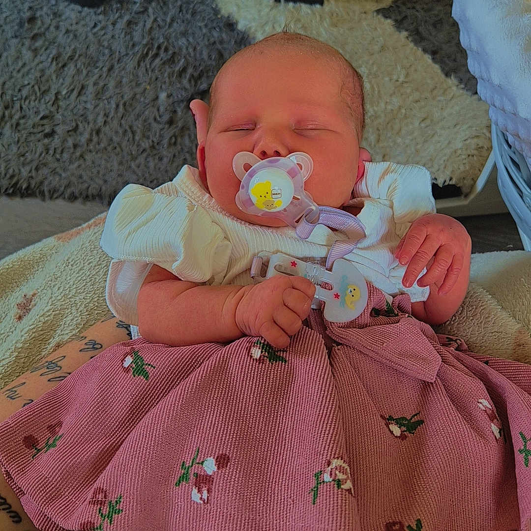 Ariella is registered to the contest to win money with this photo: baby, blanket, carpet, clothing, cute, dress, floral, foot, hand, indoors, infant, pacifier, peaceful, person, pink, portrait, rest, sleeping, soft, toddler