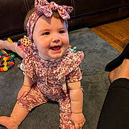 Riley joined the competition — help win amazing prizes! baby, child, smiling, sitting, portrait, floral_outfit, headband, bow, indoors, living_room, rug, leather_couch, toys, stuffed_animal, colorful, happy, infant, face, wood_floor, family_photo