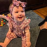 baby, child, smiling, sitting, portrait, floral_outfit, headband, bow, indoors, living_room, rug, leather_couch, toys, stuffed_animal, colorful, happy, infant, face, wood_floor, family_photo