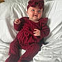 Eden-Rose joined the competition — help win amazing prizes! baby, child, infant, red_clothing, headband, bow, knitwear, bed, white_bedspread, portrait, sitting, cute, smiling, indoor, person, soft_lighting, cozy, happy, young_child, fashion