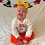 baby, child, tongue_out, yellow_bow, headband, orange_pants, white_sweater, halloween, witch_hat, garland, sitting, blanket, cute, playful, indoors, smiling, holiday_decor, chubby_cheeks, portrait, happy