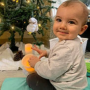 Néoh a rejoint le concours — aidez-le/la à gagner de superbes lots ! baby, child, smile, indoor, christmas_tree, holiday, decorations, lights, plush_toy, candle, floor_mat, sitting, winter, cute, festive, cozy, toy, face, person, home