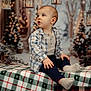 toddler, child, plaid_blanket, socks, buttoned_shirt, lanterns, holiday_decor, christmas_trees, indoors, festive, curious_expression, seated, winter_clothing, portrait, soft_lighting, background_bokeh, cozy, cute, young_child, holiday_season
