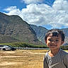 boy, car, casual_clothing, child, clouds, daylight, field, grass, happy, landscape, mountains, nature, outdoor, person, portrait, scenic, sky, smile, sunny, young