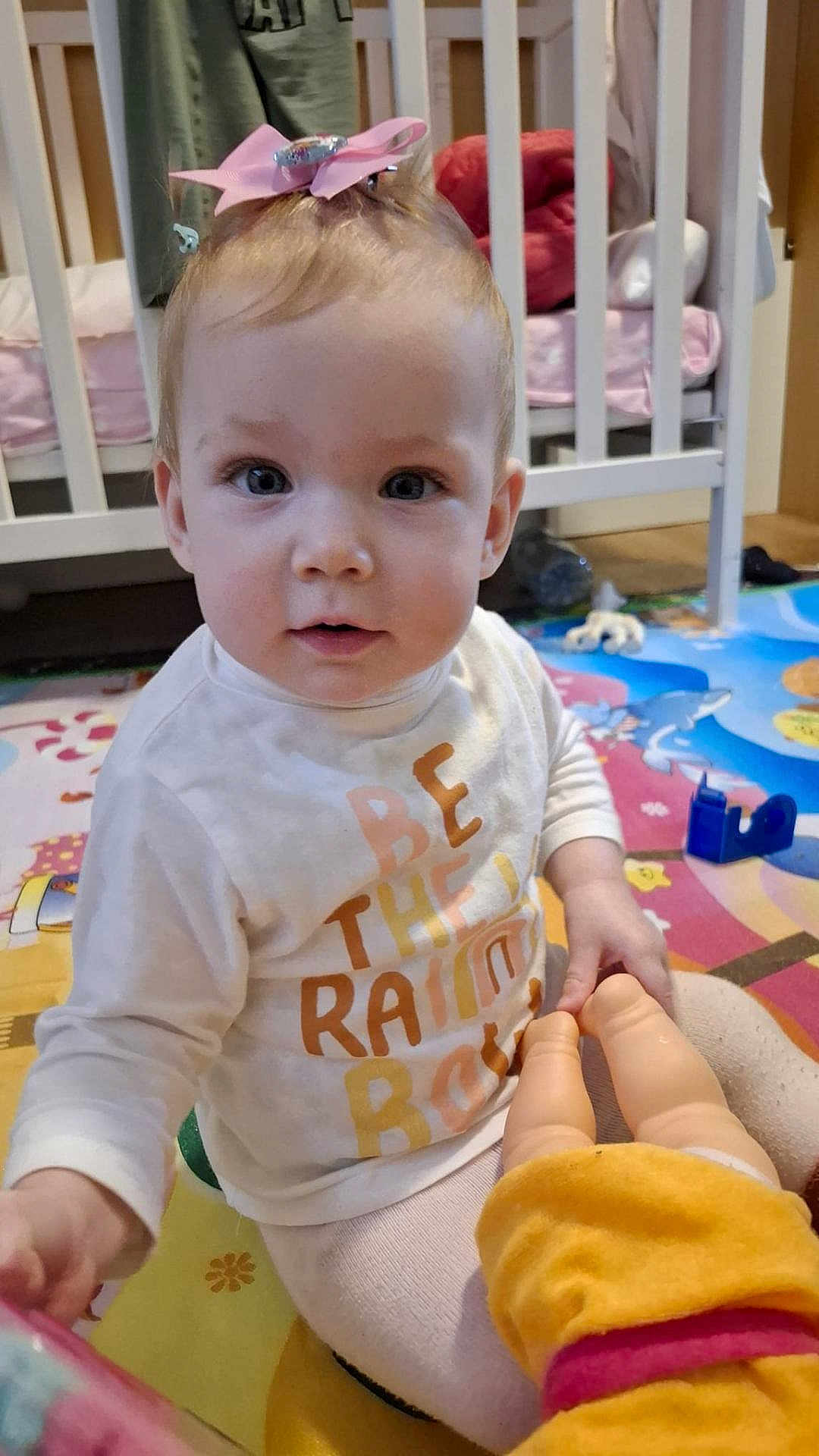 Miya Vieru participe au concours pour gagner de l'argent avec cette photo : baby, child, pink_bow, doll, toy, crib, play_mat, indoor, toddler, clothing, person, face, floor, furniture, hand, sitting, curious, nursery, colorful, young_child