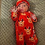 baby, child, infant, red_onesie, reindeer_pattern, hat, blanket, textured_blanket, hand_raised, lying_down, cute, holiday_theme, smiling, indoors, portrait, newborn, cozy, clothing, person, face