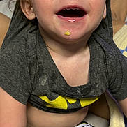 Koda is registered to the contest to win money with this photo: toddler, child, smiling, happy, batman_shirt, messy_face, food_on_chin, short_sleeves, pants, indoor, blanket, seated, person, cute, young_child, casual_clothing, light_skin, hair, cheerful, portrait