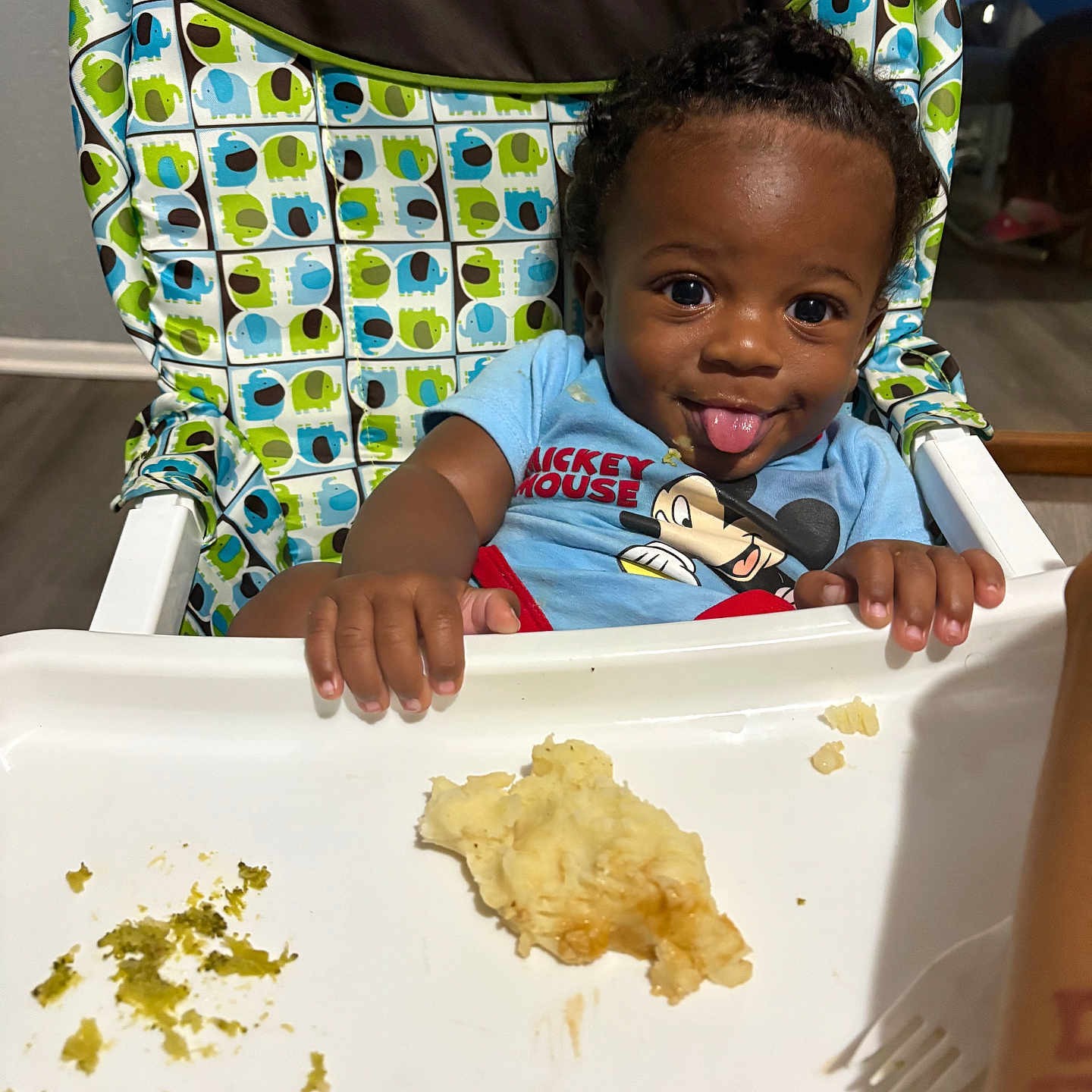 Jabari joined the competition — help win amazing prizes! toddler, high_chair, food, messy, playful, tongue_out, mickey_mouse, shirt, elephant_pattern, colorful, indoor, child, person, smile, face, hands, tray, cute, baby, meal