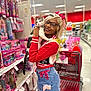 person, cat, shopping_cart, toy_aisle, dolls, retail_store, blonde_hair, glasses, septum_piercing, colorful_clothing, red_sweater, ripped_jeans, bow, pink, holding_pet, portrait, smiling, aisle, shelves, playful
