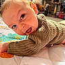 baby, infant, smiling, face, knitted_sweater, quilt, indoor, child, happy, cute, young, person, portrait, toddler, playful, cozy, bright_eyes, lying_down, colorful, warm