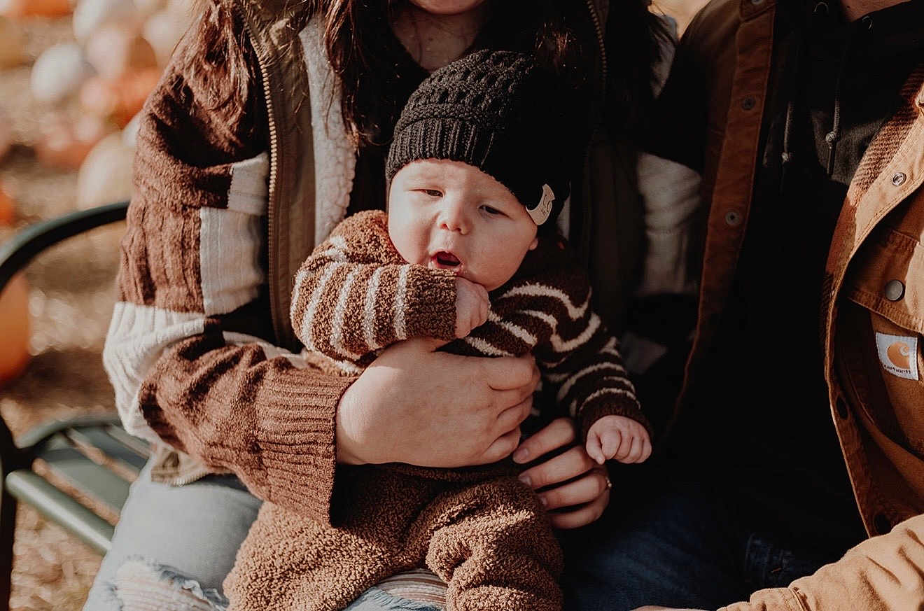 Greyson is registered to the contest to win money with this photo: baby, child, knit_hat, striped_sweater, brown_clothing, fall, autumn, outdoor, family, holding, curious_expression, warm_clothing, bench, nature, pumpkins, casual_wear, portrait, people, hands, seasonal