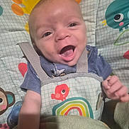 Julius is registered to the contest to win money with this photo: baby, infant, smiling, happy, seat, baby_seat, child, clothing, blue_shirt, straps, rainbow, animal_print, bird, monkey, pacifier, blanket, hand, face, portrait, indoors
