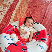 Hélios participe au concours pour gagner de l'argent avec cette photo : baby, smiling, inflatable_ring, bedspread, patterned, marine_animals, whales, sharks, indoor, child, cute, infant, clothing, happy, lying_down, hair, playful, colorful, soft_lighting, person