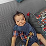 baby, bib, child, couch, cute, decorative_pillow, denim_shorts, gray_couch, happy, home, indoor, infant, pacifier, pacifier_clip, person, pillow, plaid_shirt, relaxing, sitting, smiling