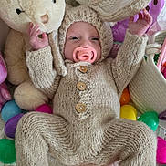 Violet is registered to the contest to win money with this photo: baby, infant, knitted_clothing, bunny_ears, pacifier, stuffed_animal, plush_toy, colorful_eggs, blanket, cute, easter_theme, child, indoors, soft_texture, smiling, lying_down, hand_raised, foot, cozy, playful
