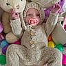 baby, infant, knitted_clothing, bunny_ears, pacifier, stuffed_animal, plush_toy, colorful_eggs, blanket, cute, easter_theme, child, indoors, soft_texture, smiling, lying_down, hand_raised, foot, cozy, playful