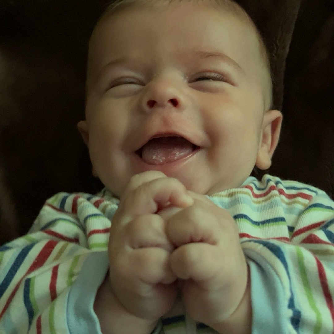 Colton is registered to the contest to win money with this photo: baby, smiling, laughing, child, infant, striped_clothing, hands, face, cute, happy, portrait, indoors, cozy, young_child, expressive, human, joy, baby_garments, sleeves, warm