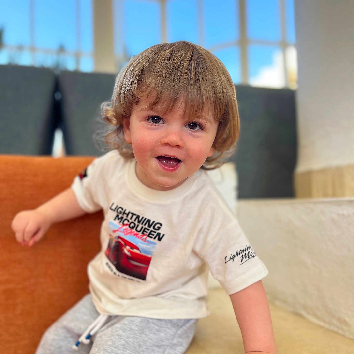 Nolan a rejoint le concours — aidez-le/la à gagner de superbes lots ! casual_clothing, child, curly_hair, cute, daylight, face, gray_shorts, hand, happy, indoor, interior, light, person, portrait, sitting, smiling, toddler, white_tshirt, window, young_child